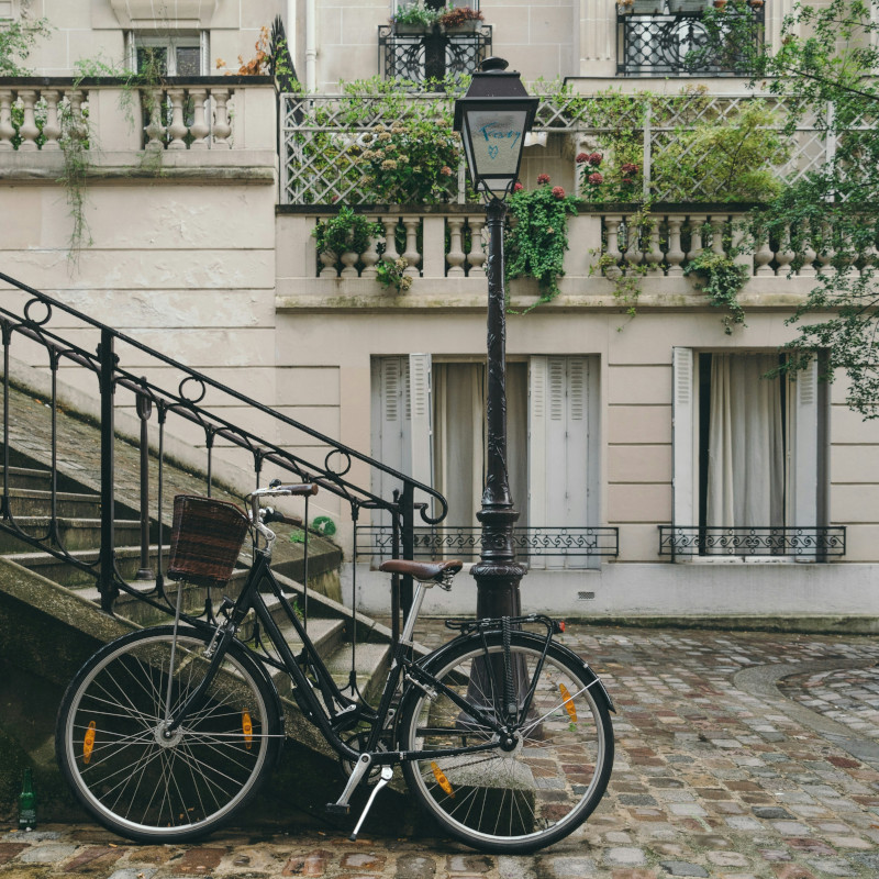 Black vintage bicycle parked by a lamppost near a stone staircase in a European courtyard.